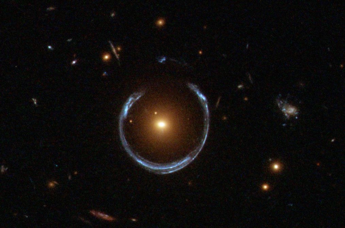 A gravitational-lensing Einstein ring photographed by Hubble: a blue ring of a distant galaxy wrapped around an orange foreground galaxy