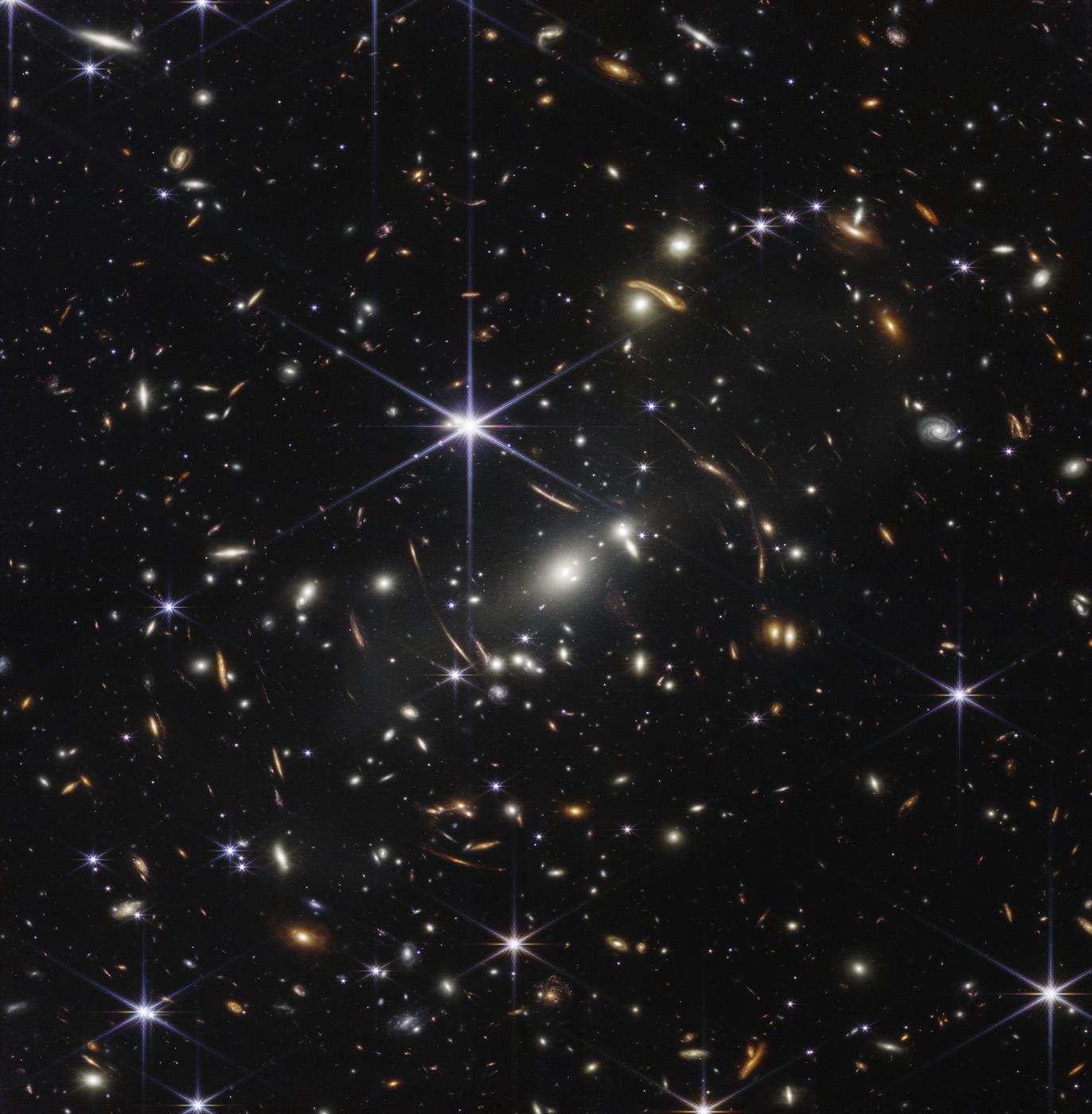 The James Webb Space Telescope's first deep field: thousands of galaxies of every shape, with arcs of more distant galaxies lensed by a foreground cluster