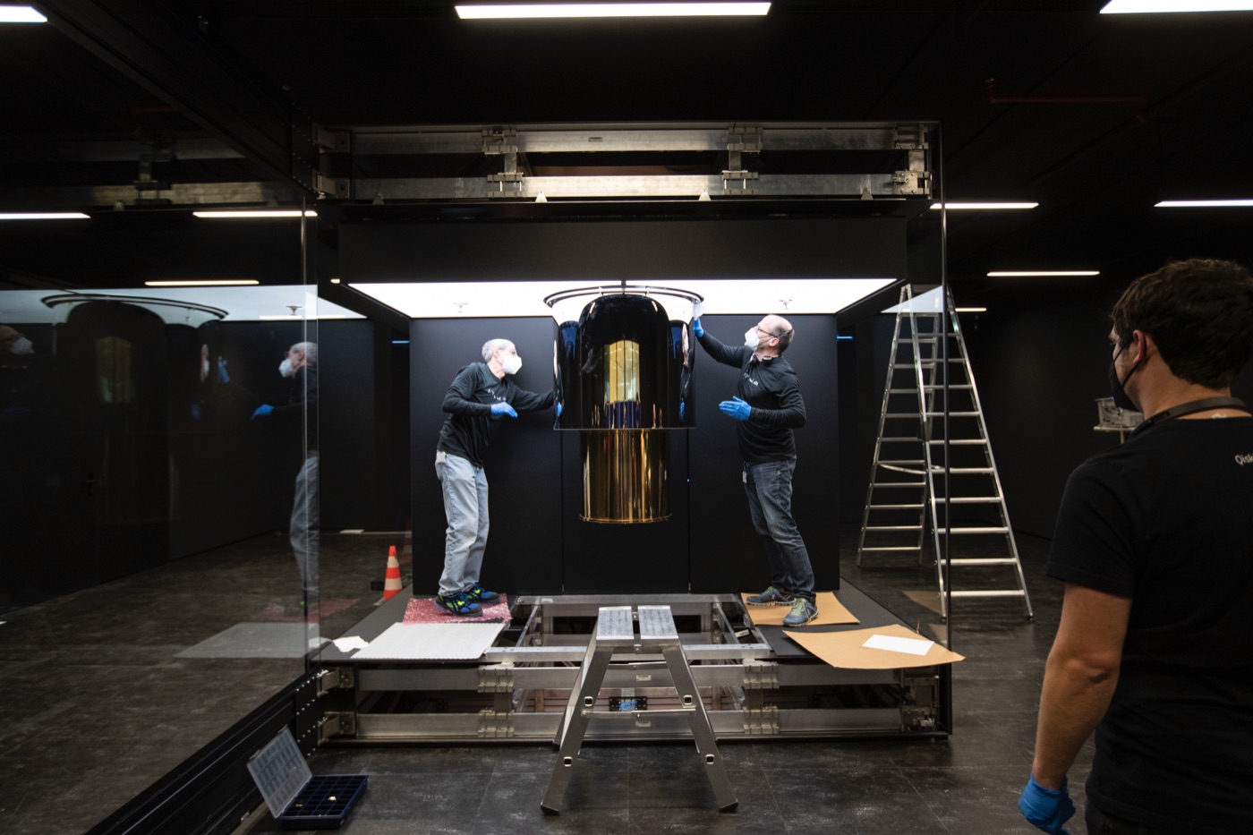 An IBM Q System One quantum computer being installed: the gold chandelier-like dilution refrigerator with technicians, inside a glass enclosure