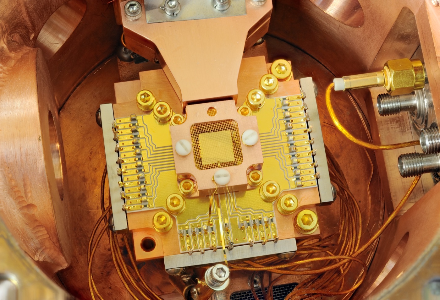 A trapped-ion quantum computing apparatus: a gold-and-copper ion-trap chip with fine wiring, mounted inside a polished copper housing